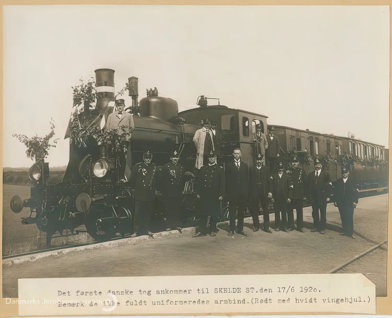 Billede af det første danske tog er ankommet til Skelde Station og jernbanepersonalet har taget opstilling for fotografering ved toget. Billede af det første danske tog er ankommet til Skelde Station og jernbanepersonalet har taget opstilling for fotografering ved toget.